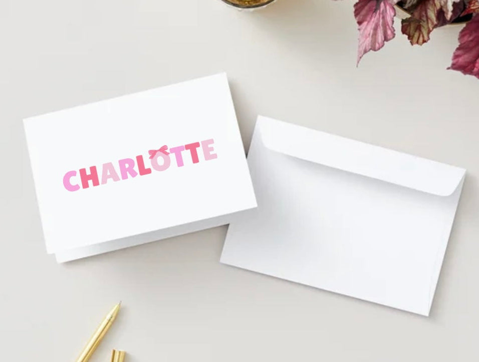 Note card with 'Charlotte' printed on it next to a white envelope on a light surface.