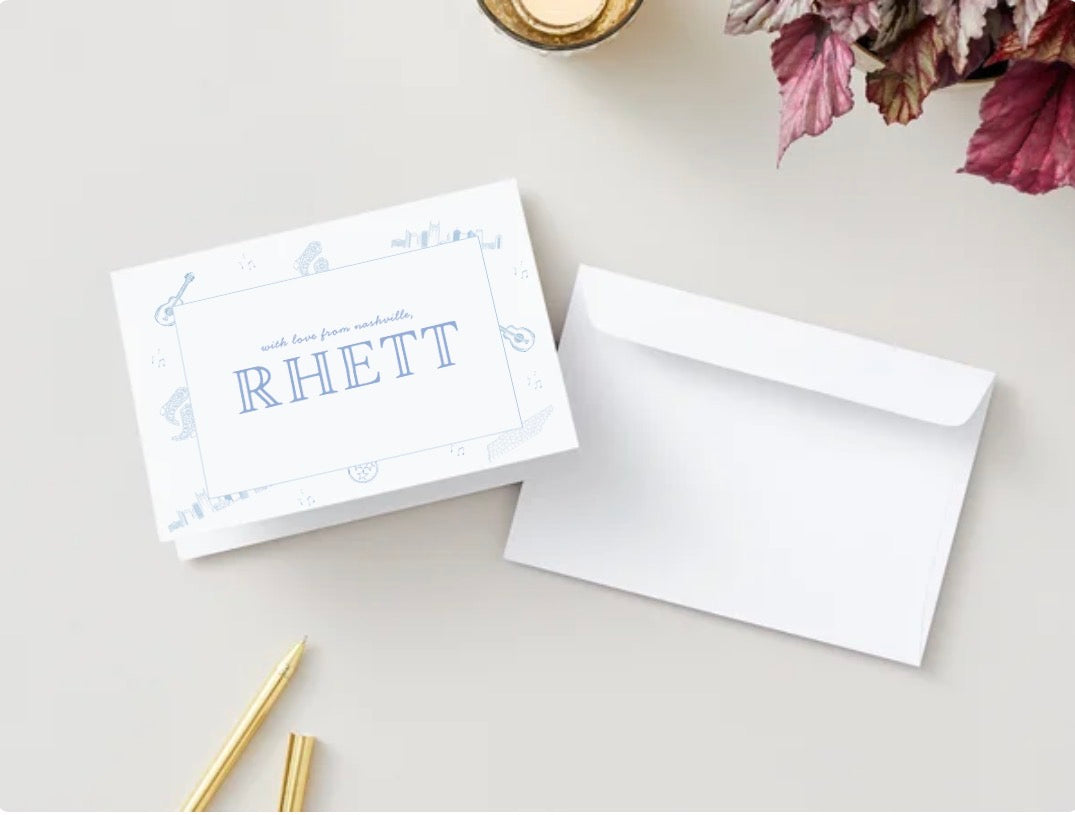 Greeting card with 'RHETT' printed on it with blue illustrations of nashville icons, accompanied by a white envelope on a light surface